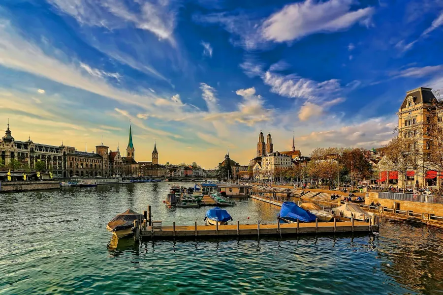 Die Zürcher Altstadt an der Limmat im Abendlicht, mit den Türmen von Fraumünster, St. Peter und Grossmünster hinter einem Bootssteg