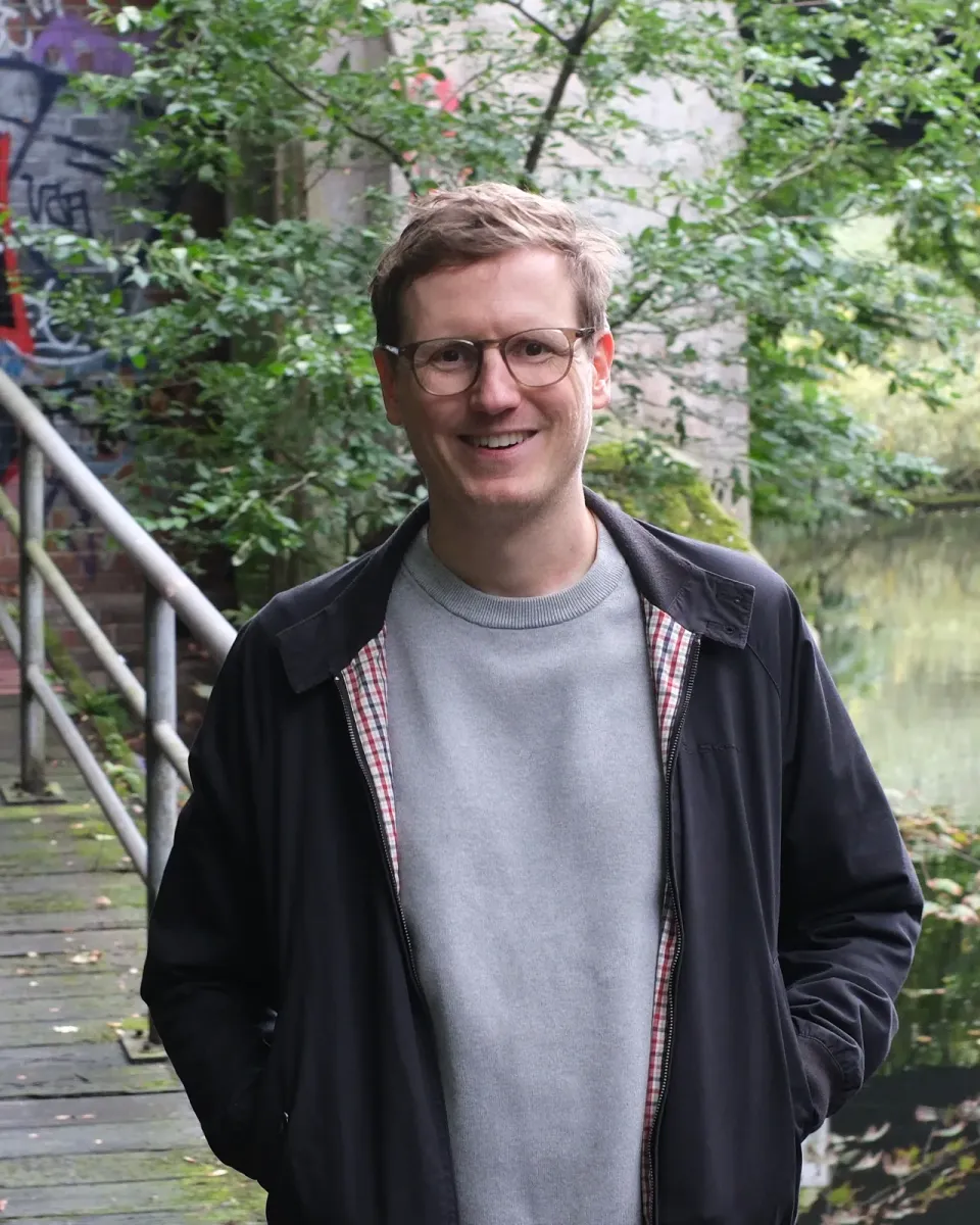 Jan Hoppe, einer der beiden Gründer von ganzheit, auf einem Holzsteg am Wasser unter einer Brücke