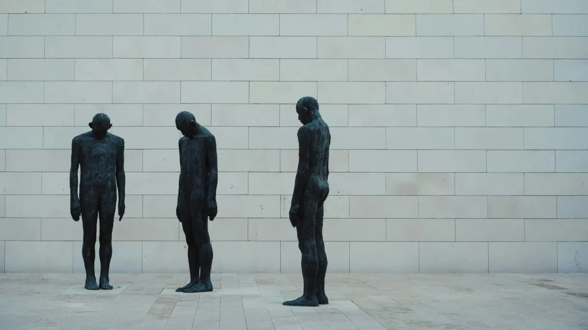 Drei Bronzefiguren stehen hintereinander vor einer hellen Steinwand